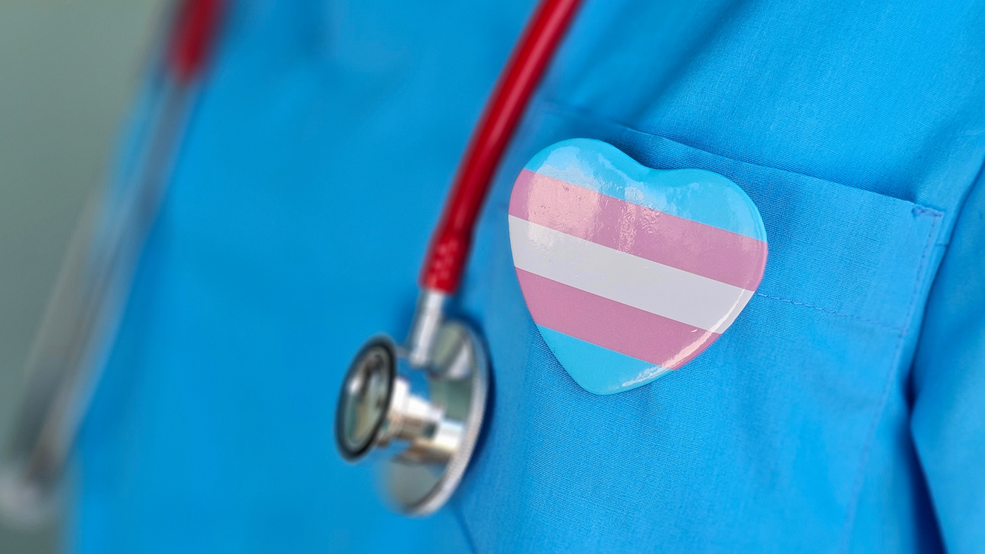 Nurse in blue scrubs wearing a heart-shaped trans flag pin